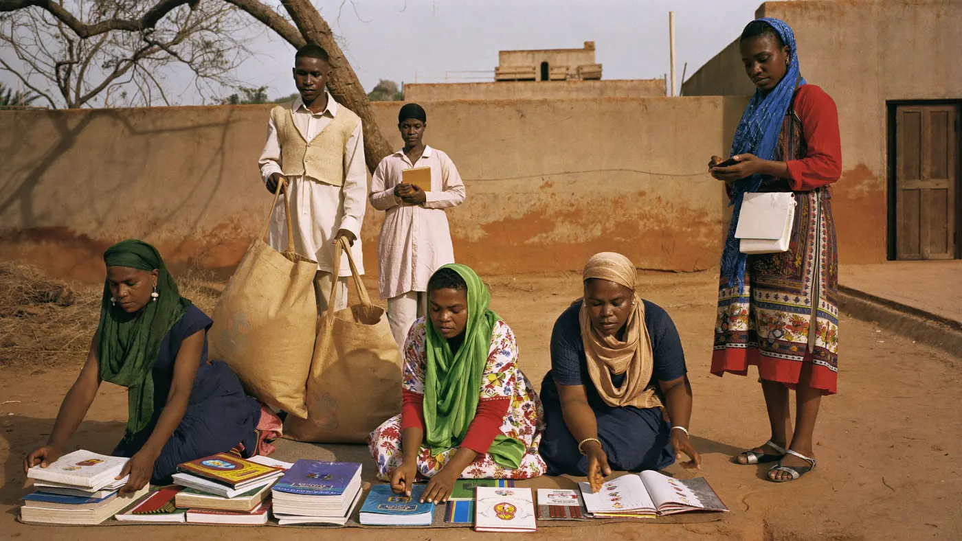 Des femmes en pagne et des hommes en boubou préparent ensemble des lots de fournitures scolaires